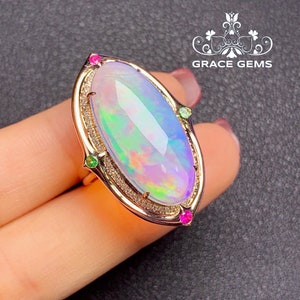 May include: A gold ring with a large oval opal gemstone surrounded by smaller diamonds. The opal has a rainbow of colors, including pink, green, and blue. The ring is accented with small green and pink gemstones.