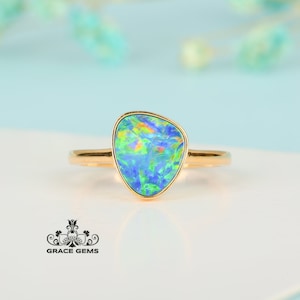May include: A gold ring with a blue, green, and iridescent opal gemstone. The opal is set in a bezel setting and has a freeform shape.