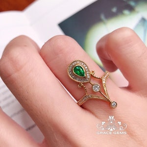 Puede incluir: Un anillo de oro con una esmeralda verde en forma de pera rodeada de diamantes m&aacute;s peque&ntilde;os. El anillo tiene un dise&ntilde;o delicado e intrincado con un arco puntiagudo.