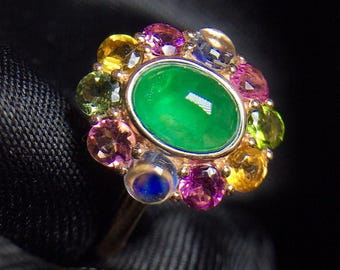 May include: A ring featuring a large green gemstone surrounded by smaller colourful gemstones. The ring is crafted from gold and has a delicate design.
