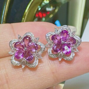Pu&ograve; includere: Un paio di orecchini d'argento a forma di fiore con pietre preziose rosa e pietre preziose bianche pi&ugrave; piccole intorno ai bordi.