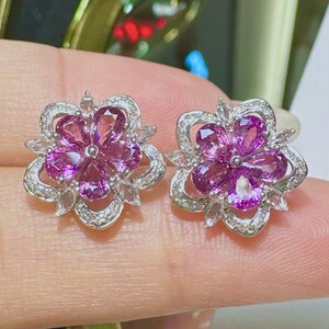 Pu&ograve; includere: Un paio di orecchini d'argento con un design floreale. Ogni orecchino presenta cinque pietre preziose rosa incastonate in un fiore d'argento con pietre bianche pi&ugrave; piccole intorno ai bordi.