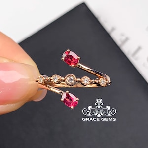 May include: A delicate gold ring with two red gemstones and a row of smaller white gemstones. The ring is designed to wrap around the finger.