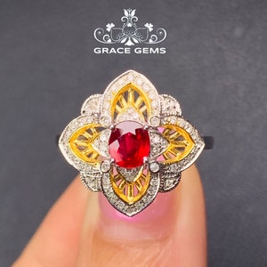 May include: A red ruby gemstone ring with a gold and white diamond floral design. The ring is set in a white metal band.