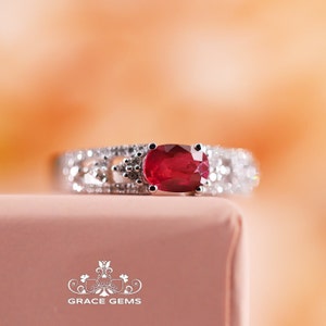 May include: A silver ring featuring a large oval ruby gemstone, surrounded by smaller diamonds. The ring is displayed against a white backdrop.