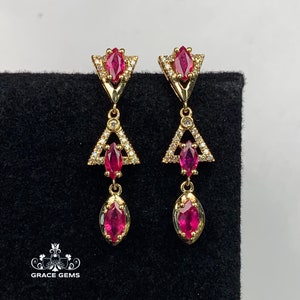 May include: Gold earrings with a geometric design featuring red ruby stones and clear cubic zirconia stones.