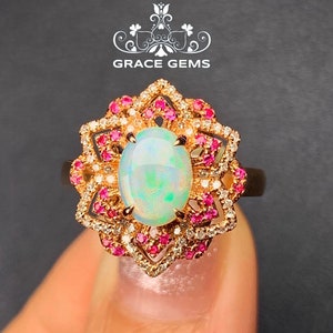 Può includere: Un anello d'oro con un grande opale ovale circondato da un'aureola di diamanti più piccoli e pietre preziose rosa. L'anello è incastonato in un design floreale.