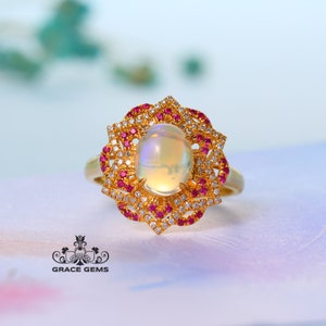 Può includere: Un anello d'oro con un grande opale ovale incastonato in un design floreale di diamanti più piccoli e rubini rossi.