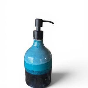 May include: A ceramic soap dispenser featuring a rounded body with a gradient colour scheme. The top section is a light turquoise, transitioning into a vibrant teal middle, and finishing with a solid black base. It has a matte black pump mechanism.