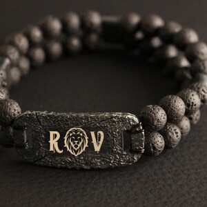 May include: Black lava rock beaded bracelet with a silver metal tag engraved with the letters "ROV" and a lion head design.