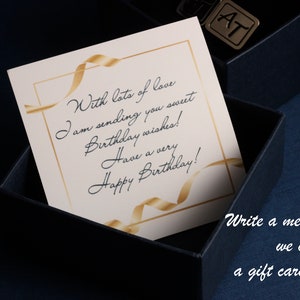 May include: A white card with gold ribbon accents and a handwritten message that reads "With lots of love I am sending you sweet Birthday wishes! Have a very Happy Birthday!" The card is inside a blue box with the letters "AT" on the top.
