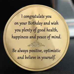 Könnte beinhalten: Eine runde Metallplakette in Gold mit einer eingravierten Botschaft: "Ich gratuliere dir zu deinem Geburtstag und wünsche dir viel Gesundheit, Glück und inneren Frieden. Sei immer positiv, optimistisch und glaube an dich selbst."