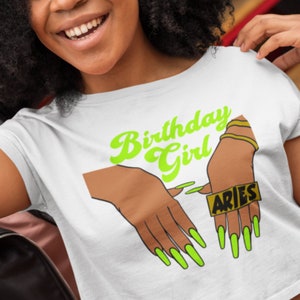 May include: White crop top with a green graphic of hands with long green nails and the text "Birthday Girl" and "Aries".