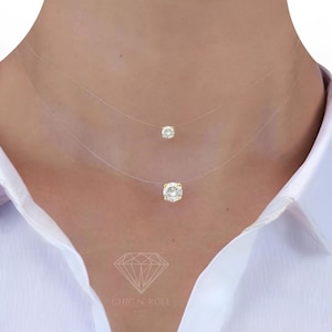 Peut inclure: Un collier délicat à deux rangs avec deux pendentifs en cristal transparent sur une fine chaîne invisible. Le collier est porté par une personne avec une chemise blanche.