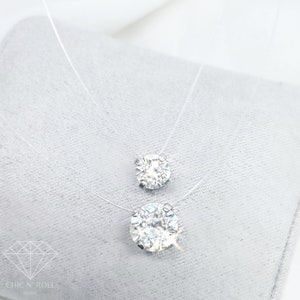 Puede incluir: Un delicado collar transparente con dos colgantes de cristal transparente redondos y brillantes. El colgante más grande está en la parte inferior del collar, y el colgante más pequeño está arriba.