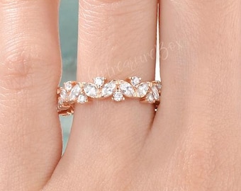 May include: A delicate gold band ring with a row of small, clear, pear-shaped stones set in a leaf-like pattern.