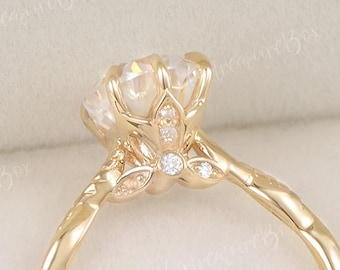 May include: A gold engagement ring with a large, round, clear gemstone. The ring features a floral design with small accent stones and a twisted band. The ring is set in a white jewelry box.