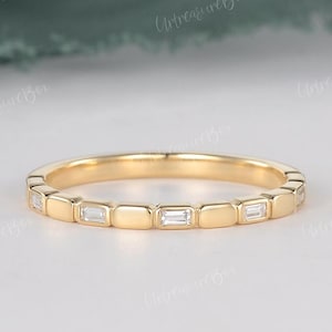 May include: A delicate gold band ring with a row of small, rectangular-shaped diamonds set in the band.
