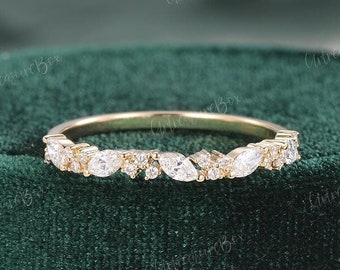 May include: A gold band ring with a cluster of clear, marquise-cut and round-cut gemstones. The ring is set against a dark green velvet background. The gemstones are arranged in a delicate, organic pattern.