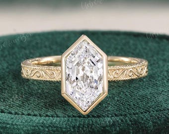 May include: A gold ring with a large, hexagonal, clear gemstone. The band features an ornate, engraved design. The ring is set against a dark green velvet surface. The text "UntreasureBox" is visible in the image.
