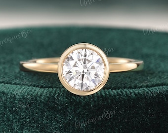 Puede incluir: Un anillo de oro con una gema transparente de talla brillante redonda engastada en un bisel liso. La banda es de oro pulido con un diseño sencillo y fino. El texto "ArtreasureBox" es visible varias veces en toda la imagen.