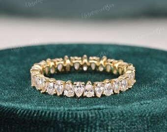 May include: A gold band ring with a pear-shaped diamond eternity band. The ring is set on a green velvet background.
