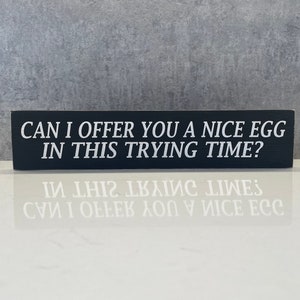 Może przedstawiać: Czarny drewniany znak z białym tekstem, który brzmi: "Czy mogę zaoferować ci miłe jajko w tym trudnym czasie?"