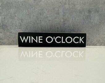 以下が含まれることがあります： 「WINE O'CLOCK」と白文字で書かれた黒い長方形の看板です。