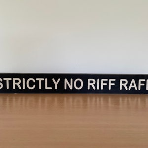 Op de afbeelding: Een zwart houten bord met witte letters met de tekst "STRICTLY NO RIFF RAFF".
