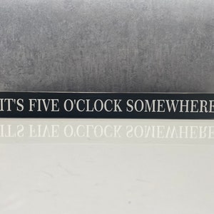 May include: Black wooden sign with white text that reads "It's Five O'Clock Somewhere".