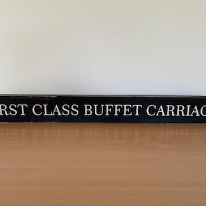 Könnte beinhalten: Schwarzes Holzschild mit weißem Text, der "FIRST CLASS BUFFET CARRIAGE" lautet.