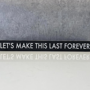 May include: A rectangular black wooden sign with the white text "LET'S MAKE THIS LAST FOREVER". The sign is displayed on a white surface with a gray background.