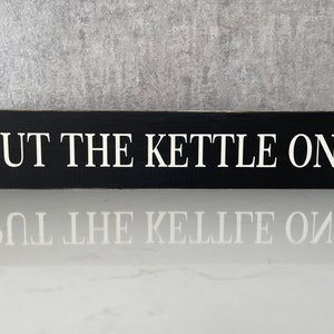 Peut inclure: Une pancarte en bois noir avec du texte blanc qui dit "PUT THE KETTLE ON".