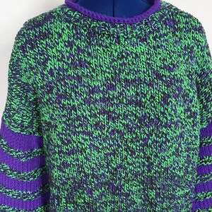 May include: A green and purple knitted sweater with striped sleeves. The sweater is made of a chunky yarn and has a relaxed fit.
