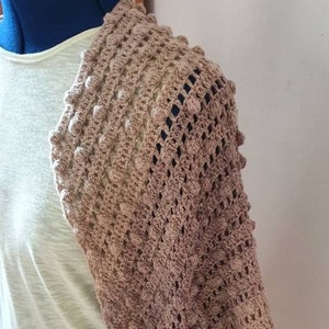 May include: A brown crocheted shawl with a textured pattern. The shawl is draped over a mannequin and has a light brown color gradient.