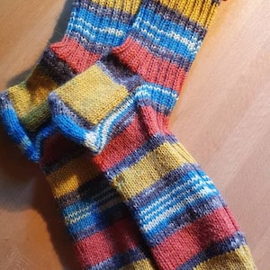 May include: A pair of striped socks in shades of red, yellow, blue, and gray. The socks are knitted and have a ribbed cuff.