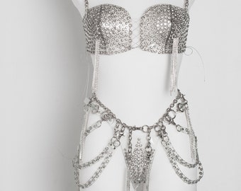 May include: A silver-toned lingerie set with a bra and a belt. The bra and belt are made of chains and rhinestones.