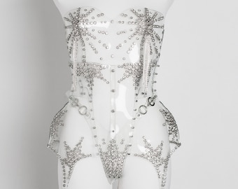 May include: A clear plastic corset with a starburst design and silver rhinestones. The corset has a halter neck strap and a matching garter belt with dangling rhinestone chains.