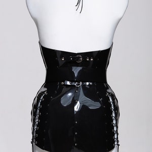 May include: Black patent leather corset with a halter neckline, a silver buckle, and lace-up sides. The corset is on a white mannequin.