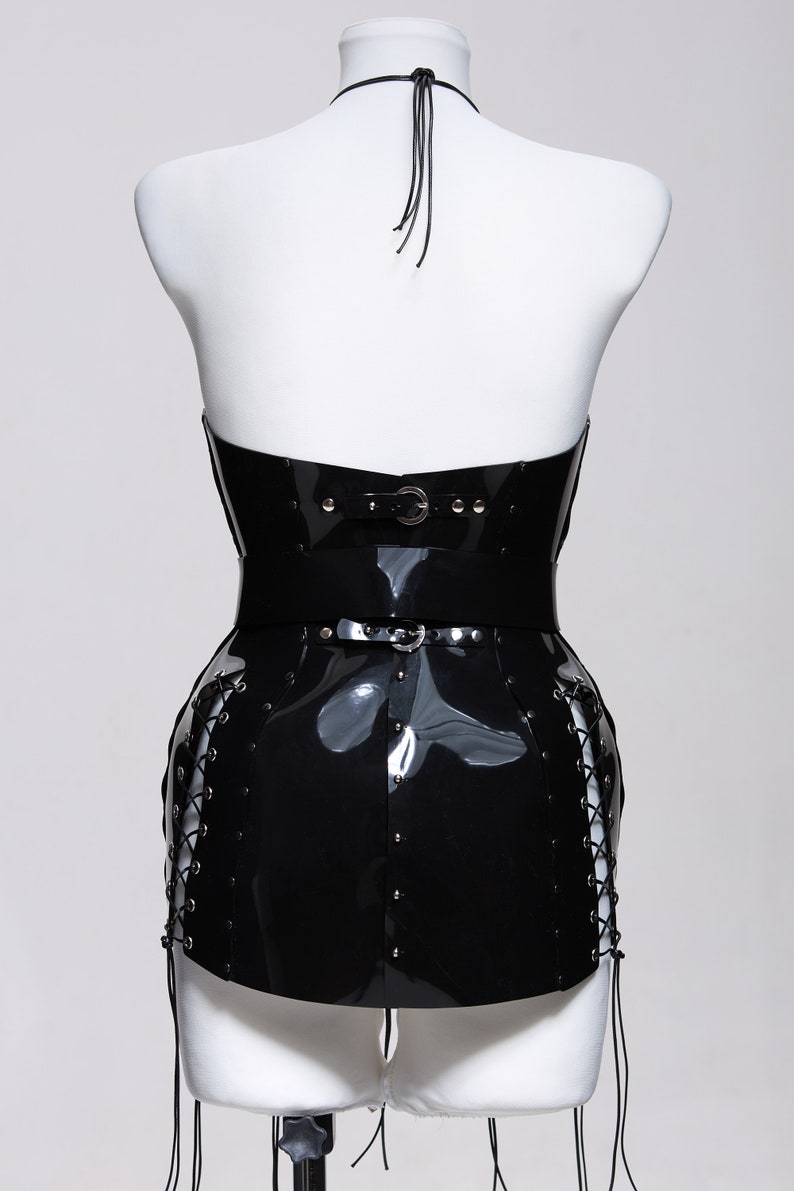 May include: Black patent leather corset with a halter neckline, a silver buckle, and lace-up sides. The corset is on a white mannequin.