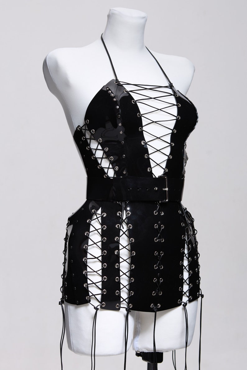 May include: A black patent leather mini dress with a lace-up bodice and a matching belt. The dress has a halter neckline and a fitted silhouette.