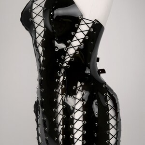 May include: A black patent leather mini dress with a lace-up design and silver grommets. The dress has a halter neckline and a fitted silhouette.