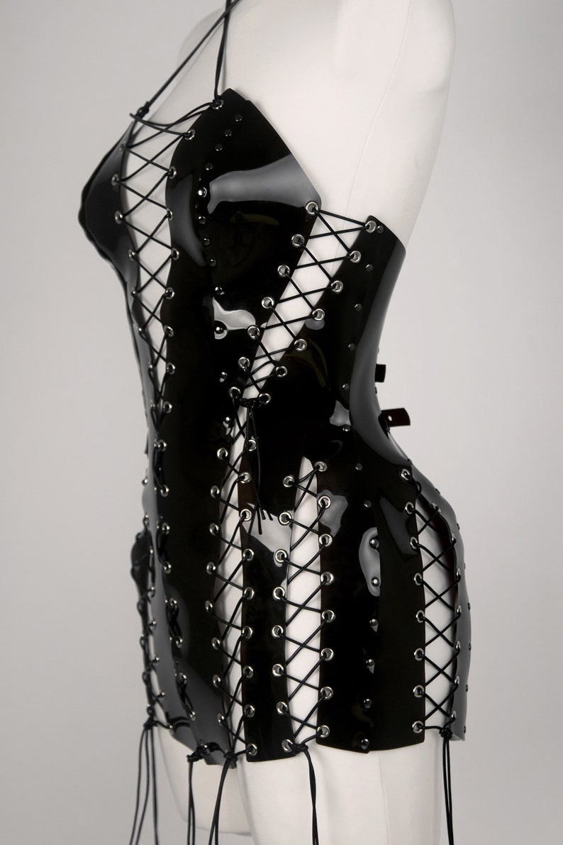 May include: A black patent leather mini dress with a lace-up design and silver grommets. The dress has a halter neckline and a fitted silhouette.