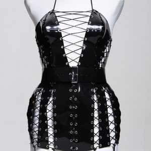 May include: A black patent leather halter dress with a lace-up bodice and skirt. The dress has a black leather belt with a silver buckle.