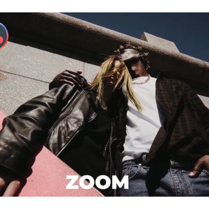 K&ouml;nnte beinhalten: Ein Paar steht zusammen, einer mit einer schwarzen Lederjacke und der andere mit einer braunen karierten Jacke. Ein rosa Skateboard befindet sich im Vordergrund. Das Wort "ZOOM" steht in wei&szlig;en Blockbuchstaben. Der Himmel ist tiefblau.