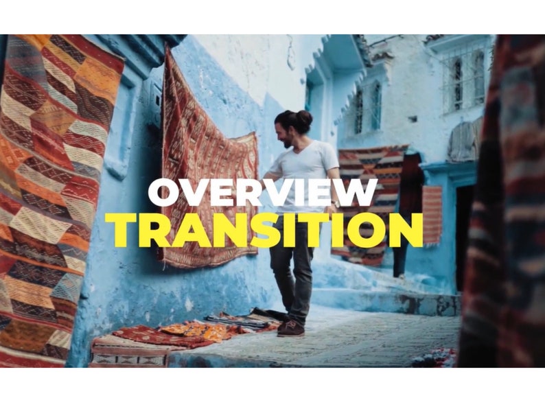 K&ouml;nnte beinhalten: Ein Mann steht in einer blau get&uuml;nchten Gasse, umgeben von bunten Teppichen und Textilien. Das Bild zeigt den Text "OVERVIEW TRANSITION" in gro&szlig;en gelben Buchstaben. Die Szene deutet auf einen Markt oder eine Werkstatt hin.