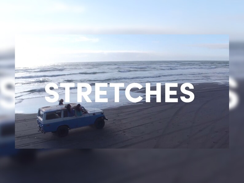 May include: A blue and white vintage SUV drives on a dark sandy beach with the word "STRETCHES" in white text across the image. The ocean and sky are visible in the background.