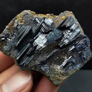 May include: A dark blue and black mineral specimen with a rough, textured surface. The mineral has a layered, striated appearance with a metallic sheen.
