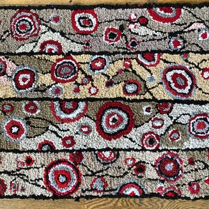 May include: A hand-woven rug with a geometric pattern of red, white, and gray circles on a beige background. The rug is made of wool and has a textured surface.