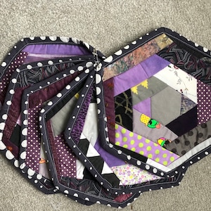 Könnte beinhalten: Ein Set aus acht sechseckigen, gesteppten Tischsets in Lila und Schwarz mit weißen Punkten. Die Tischsets bestehen aus verschiedenen Stoffen und sind im Patchwork-Stil zusammengenäht.